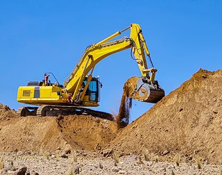 Heavy-duty yellow excavator digging soil on a clear day.